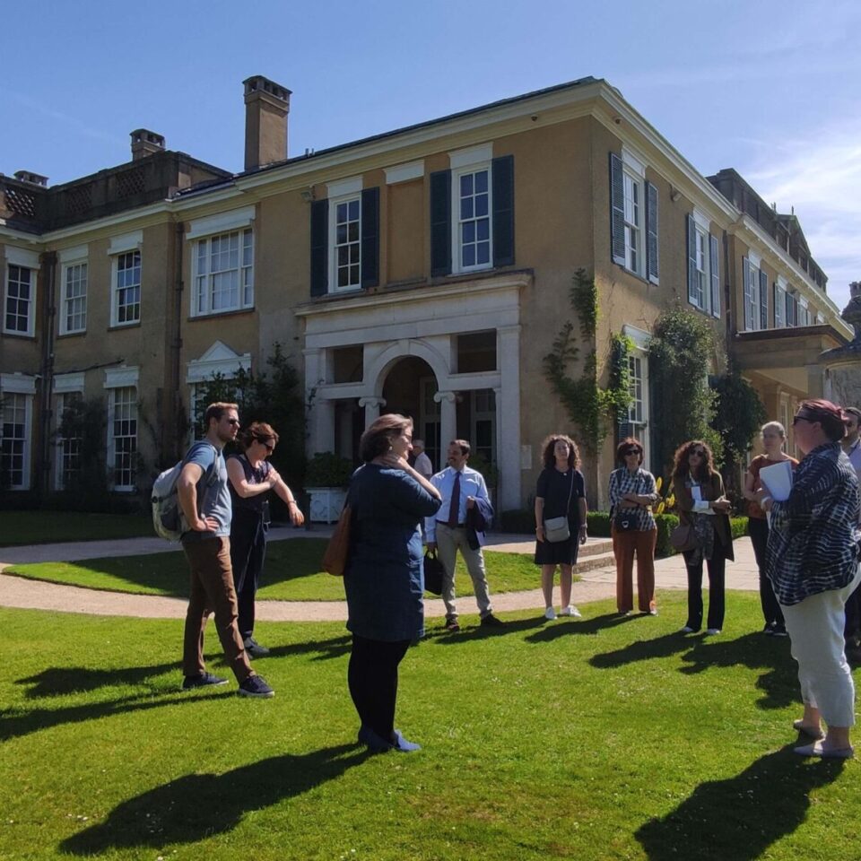 a group of people talking on a lawn in front of a grand house