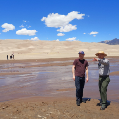 two men in front of a sand dune on a TAP INTO funded exchange