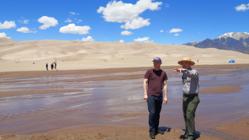 two men in front of a sand dune on a TAP INTO funded exchange