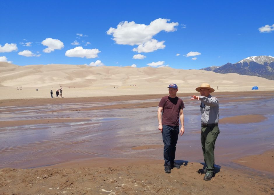 two men in front of a sand dune on a TAP INTO funded exchange