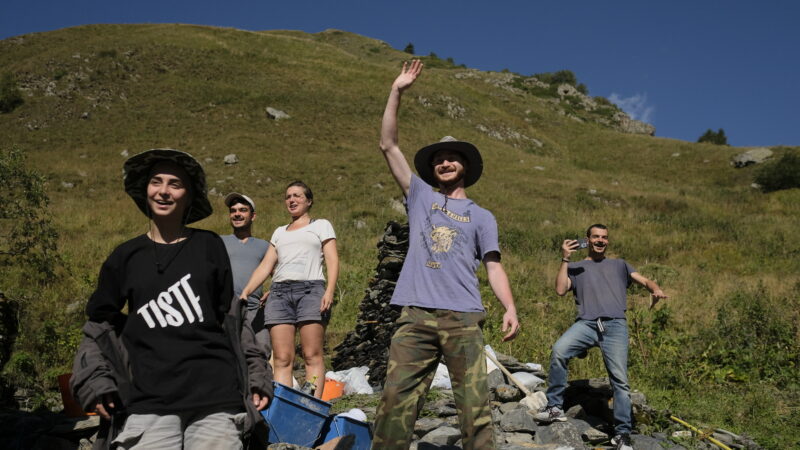 a group of people on a grassy hillside, one waving, heritage for peace project in Georgia