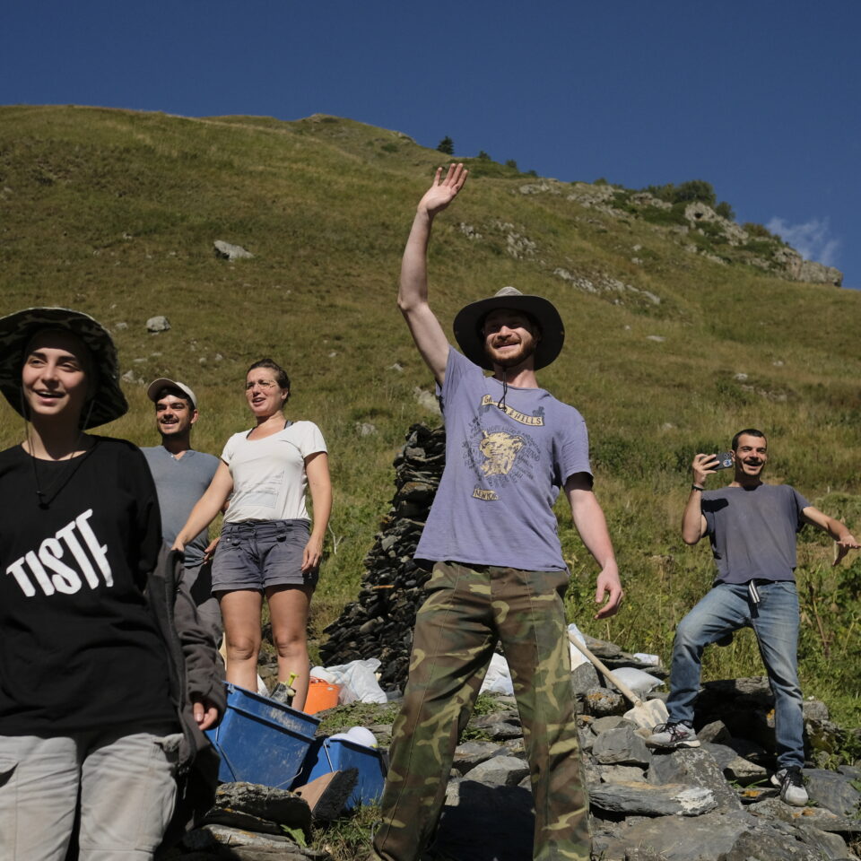 a group of people on a grassy hillside, one waving, heritage for peace project in Georgia