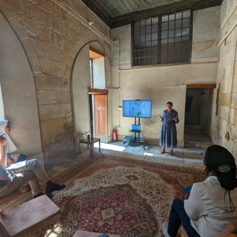 a woman giving a presentation on a screen to 2 people seated in Bayt Al Razzaz, Cairo