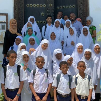 A group of school children in Zanzibar smiling at the camera outside a grand doorway