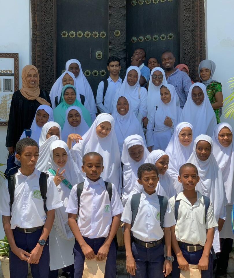 A group of school children in Zanzibar smiling at the camera outside a grand doorway