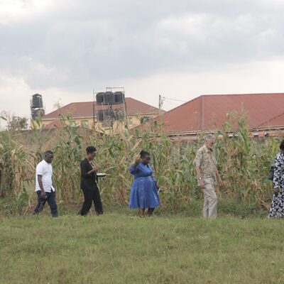 evaluation visit - a small group of people walking in a green field in Uganda