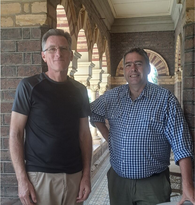 two men smiling at the camera under a brick archway at Rippon Lea estate