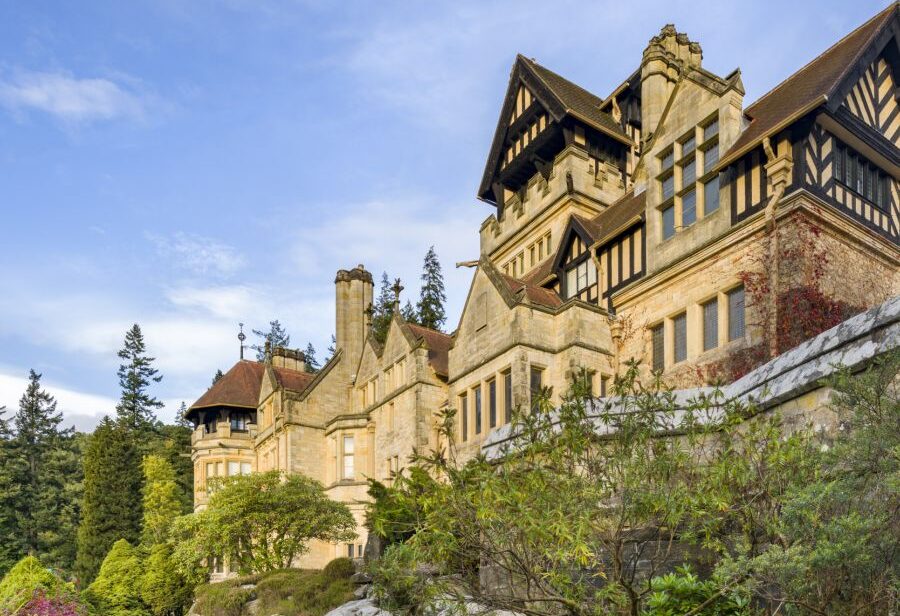 Looking up a Cragside House from a rocky path which falls steeply below the building