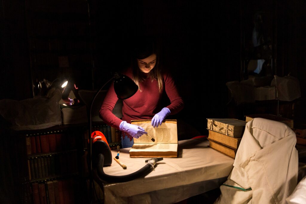 a paper conservator brushing an antique book under a lamp