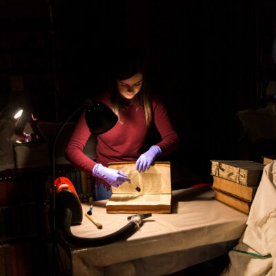 a paper conservator brushing an antique book under a lamp