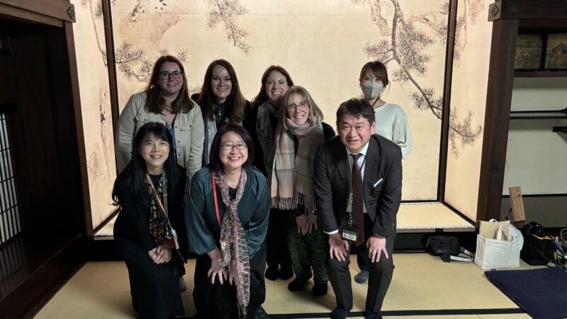 a group of people smiling at the camera in a Japanese room with a screen decorated with Japanese foliage. One of the group is part of TAP INTO grant awarded