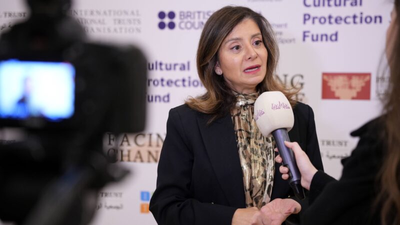 a photo of HRH Princess Dana Firas of Jordan, speaking into a microphone being interviewed by a tv crew - the camera is just visible