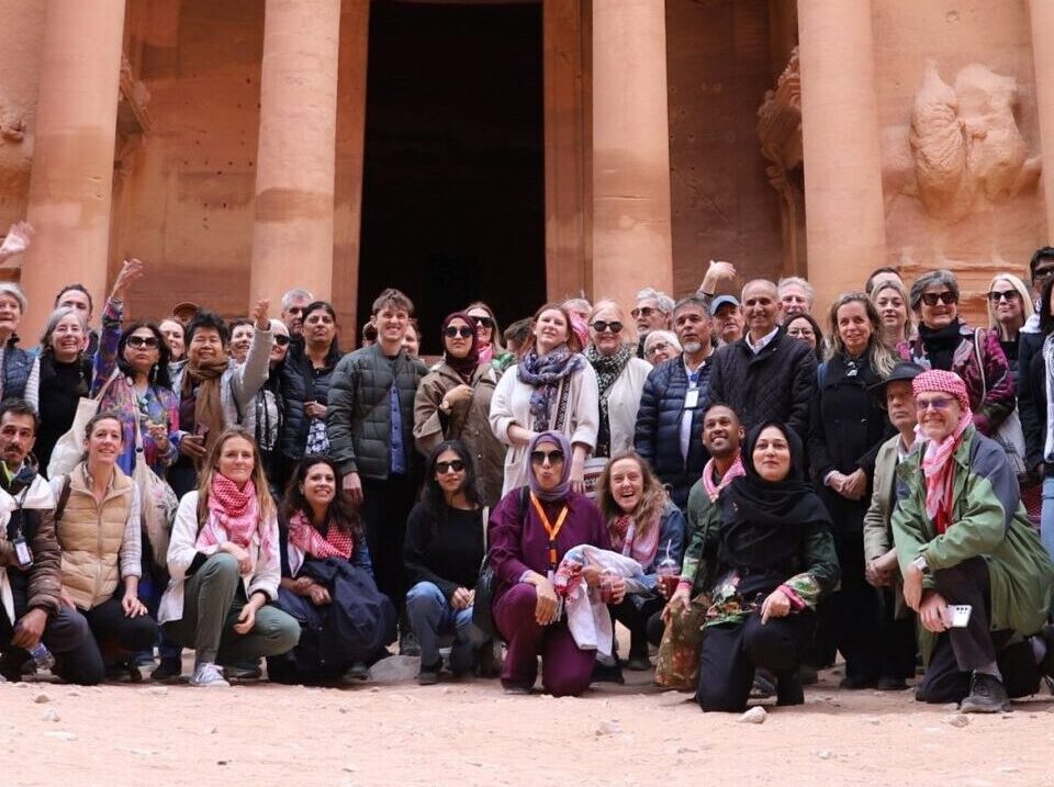 a large group of people smiling at the camera in front of The Treasury, a large temple carved from red stone in Petra, Jordan