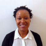 a photo of a woman smiling. She is wearing a white shirt and black cardigan and standing by a plain white wall