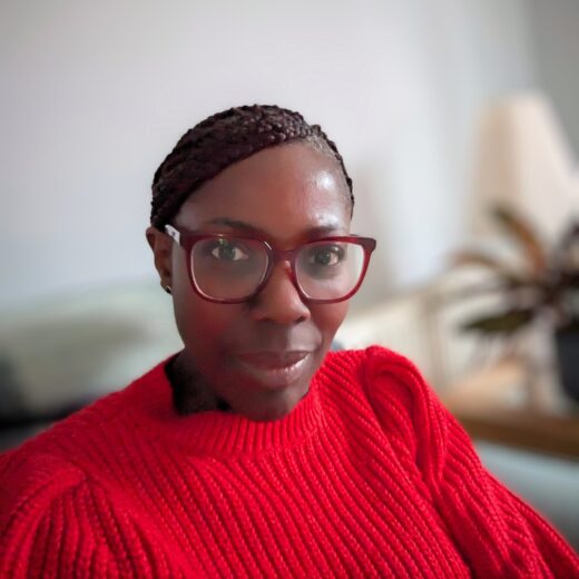 portrait photo of a woman looking straight at the camera. She is wearing glasses and a very vivid red top.