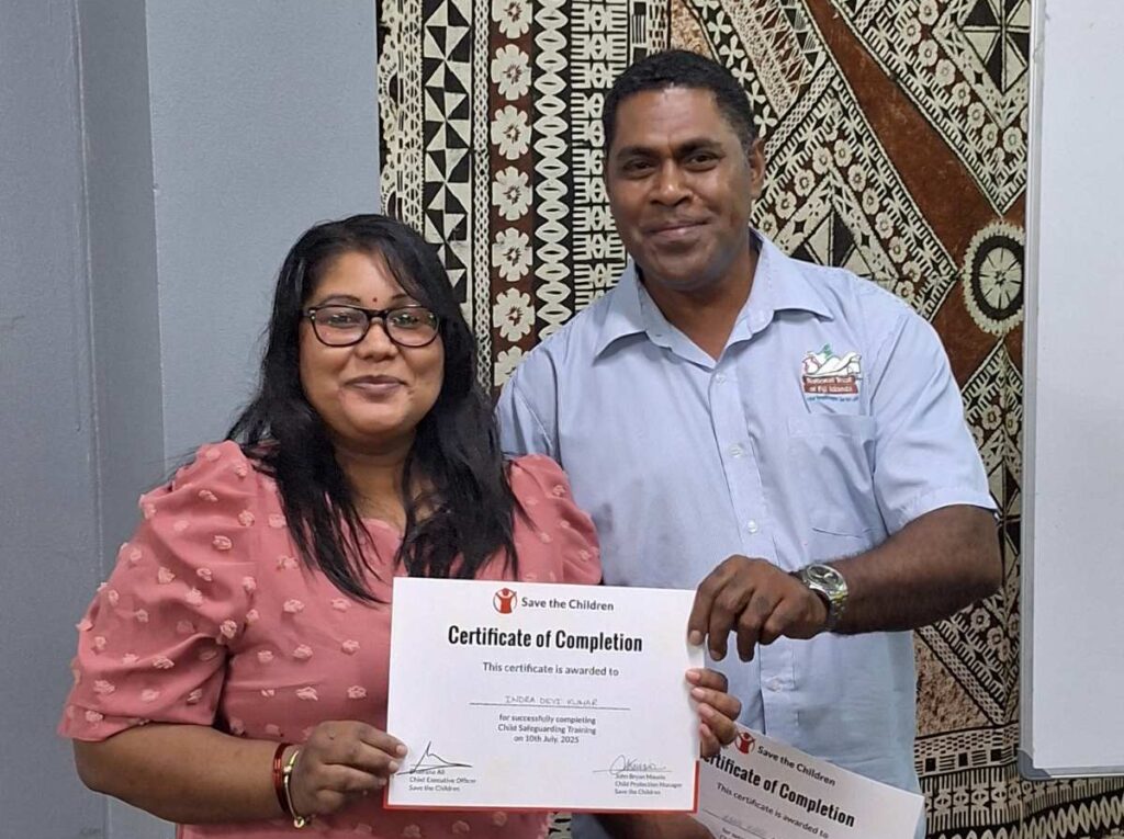 a man and a woman presenting a certificate in front of an elaborate textile backdrop from Fiji
