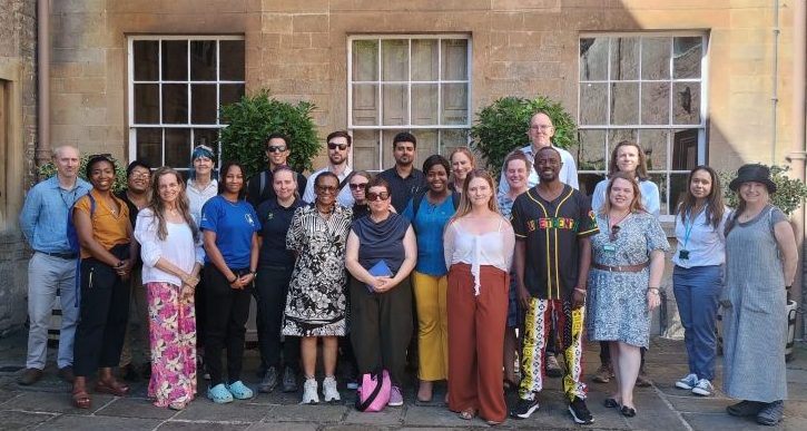 a group of people in a formal pose smiling at the camera. They are standing in front of 3 large windows which are part of an historic house at Dyrham Park and meeting for the INTO RISE programme