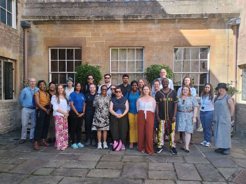 a group of people in a formal pose smiling at the camera. They are standing in front of 3 large windows which are part of an historic house at Dyrham Park and meeting for the INTO RISE programme