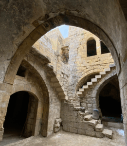 the interior of an historic house in As-Salt, Jordan made of distinctive yellow stone this image shows arches and stone staircases, with a peek of blue sky. This site is managed by Petra National Trust