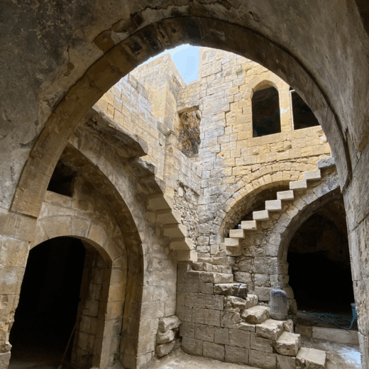 the interior of an historic house in As-Salt, Jordan made of distinctive yellow stone this image shows arches and stone staircases, with a peek of blue sky. This site is managed by Petra National Trust
