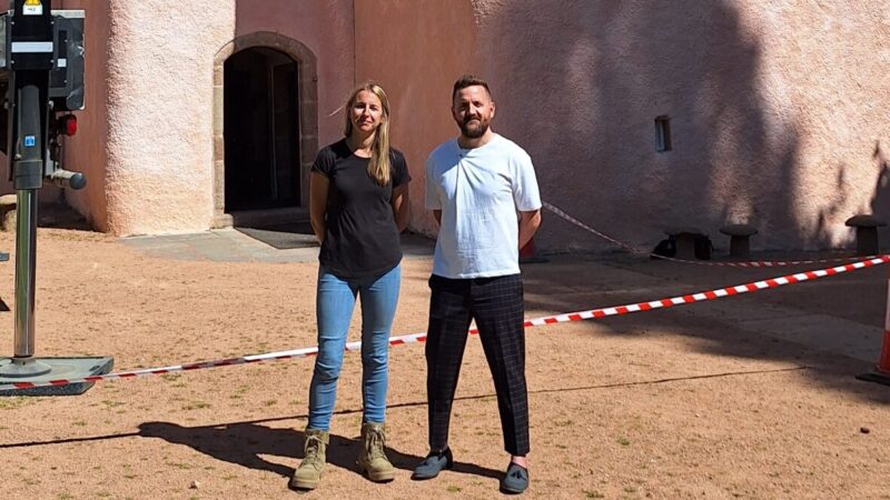 a woman and a man standing in front of a very tall pink rendered castle