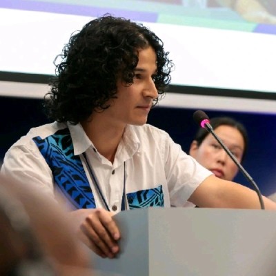 a young man with dark shoulder length hair speaking at a lectern