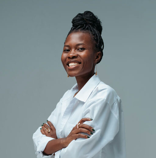 a photo of a young black woman in a white shirt. She has a bright smile and braids in a high bun