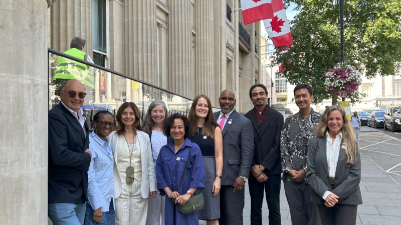 a group of people smiling at the camera outside Canada House in London, which is decorated with several large Canadian red and white flags