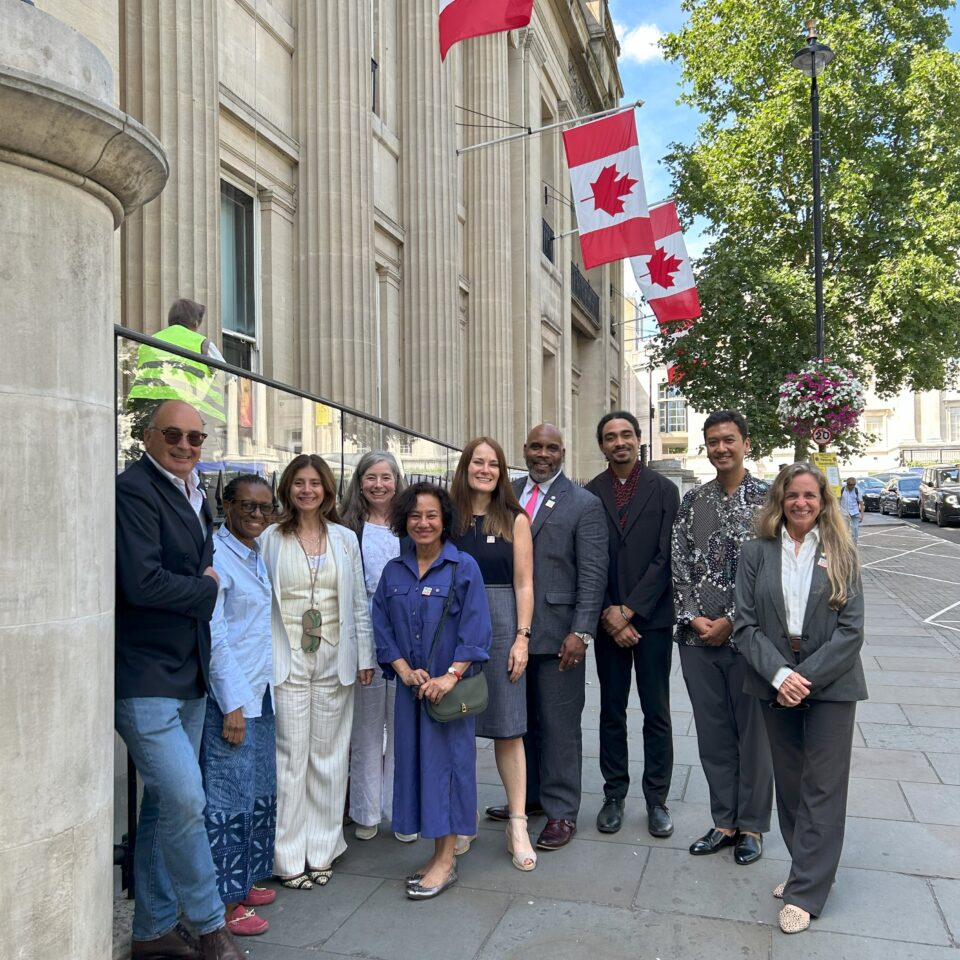 a group of people smiling at the camera outside Canada House in London, which is decorated with several large Canadian red and white flags