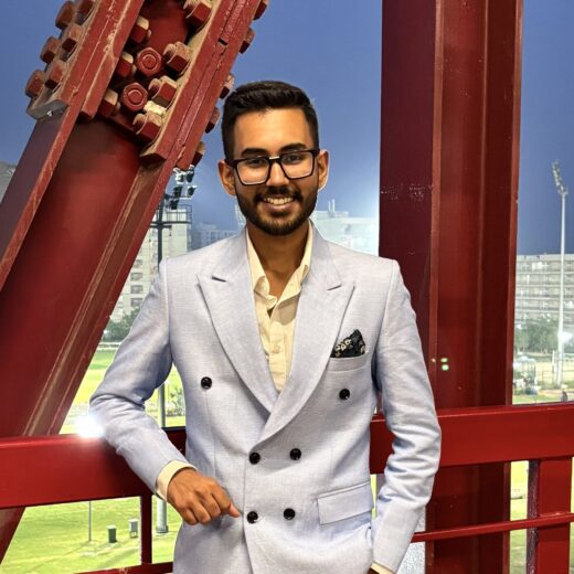 a photo of a young Indian man wearing a smart jacket and black spectacles