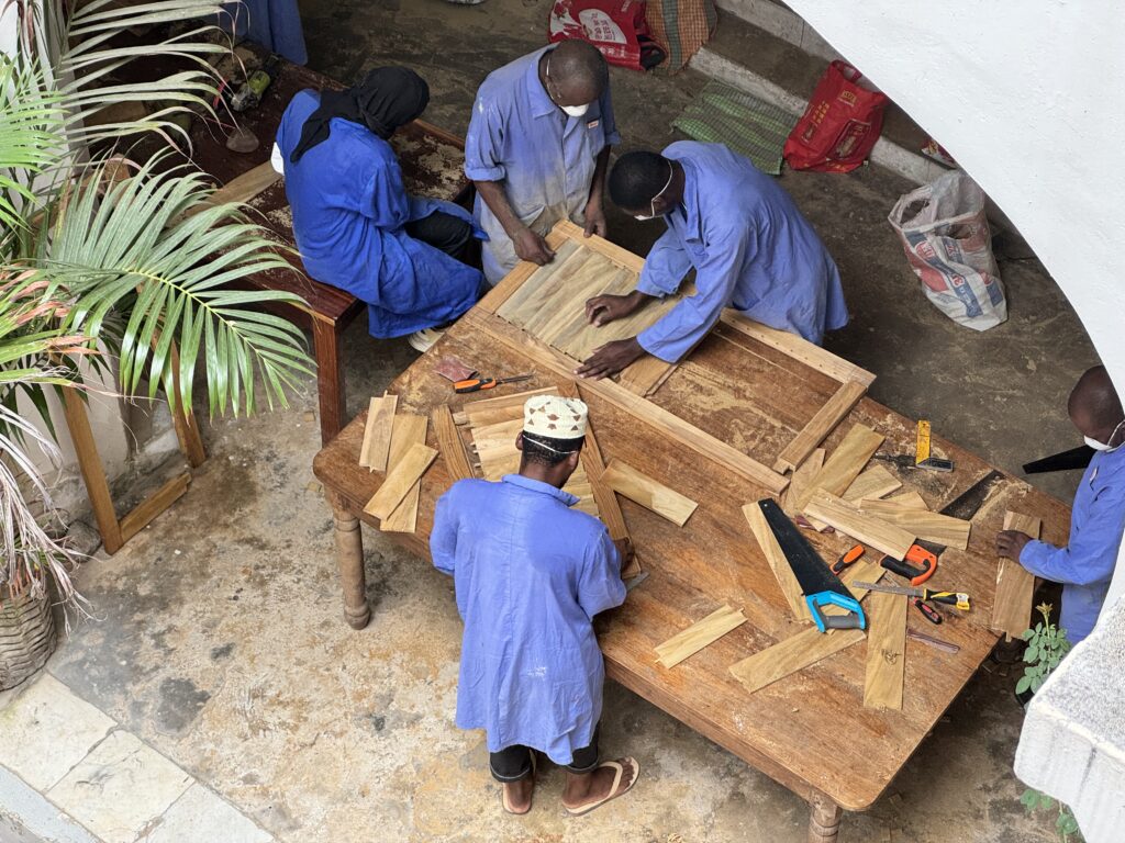 workers in blue overalls seen from above - they are repairing wooden shutters for the Old Customs House in Zanzibar