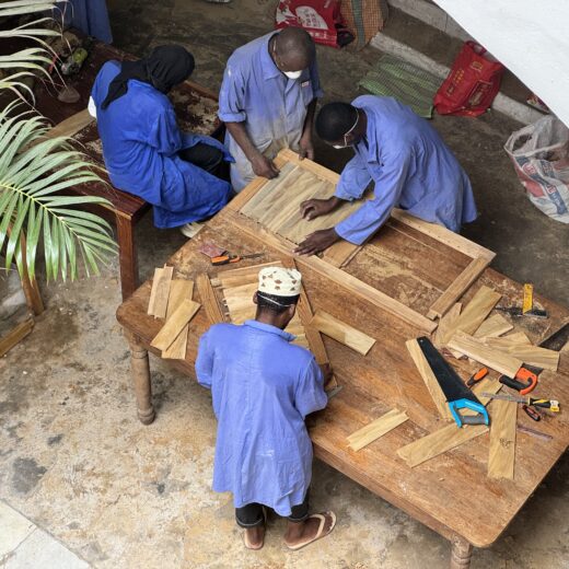 workers in blue overalls seen from above - they are repairing wooden shutters for the Old Customs House in Zanzibar