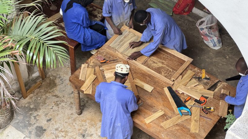 workers in blue overalls seen from above - they are repairing wooden shutters for the Old Customs House in Zanzibar