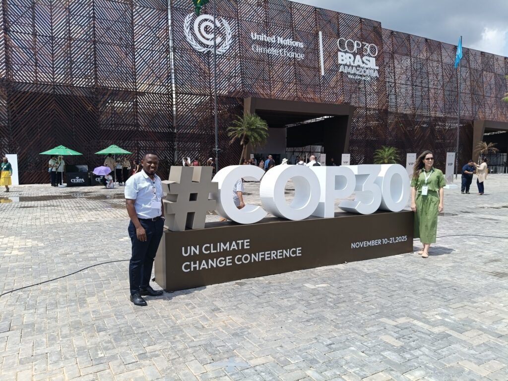 a man and woman standing beside a huge sign which reads #COP30 outside the conference venue in Brazil
