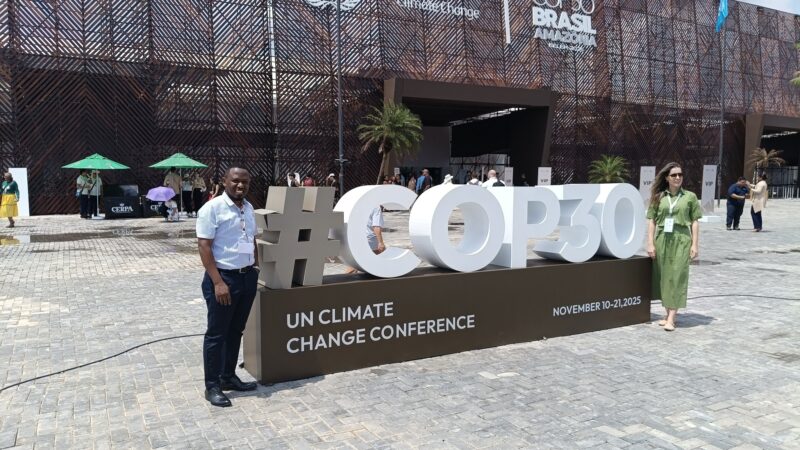 a man and woman standing beside a huge sign which reads #COP30 outside the conference venue in Brazil