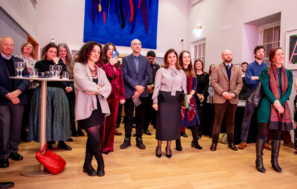 People talking at an exhibition in a high-ceilinged white room, with colourful exhibition panels