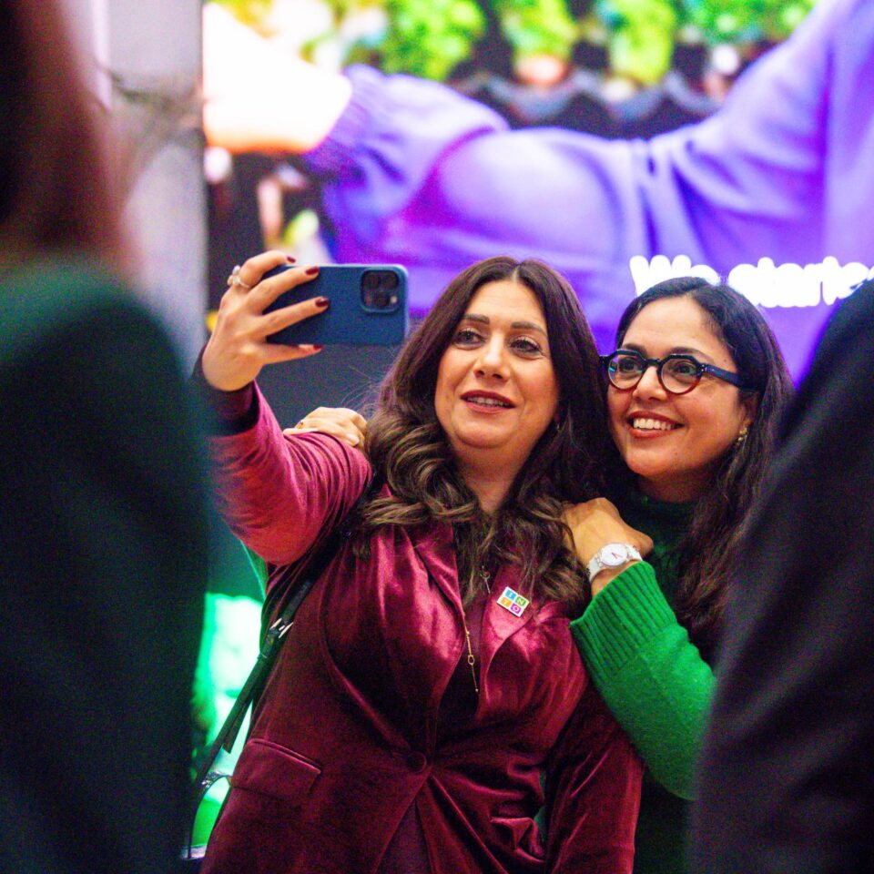 two women taking a selfie in front of a large video screen