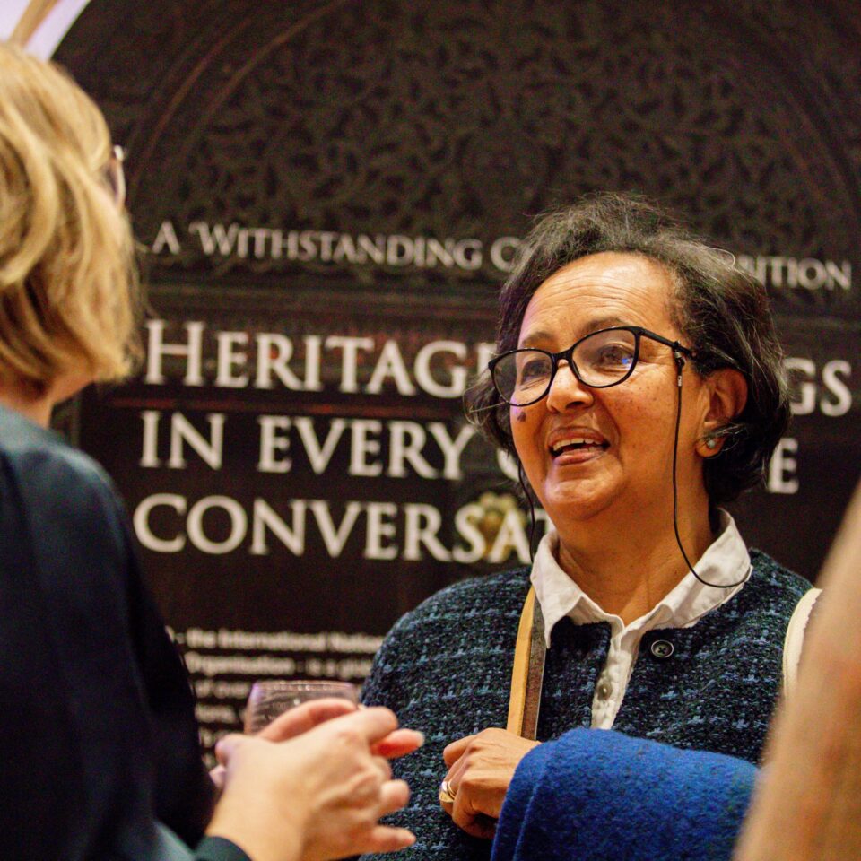 People talking at an exhibition in a high-ceilinged white room, with colourful exhibition panels