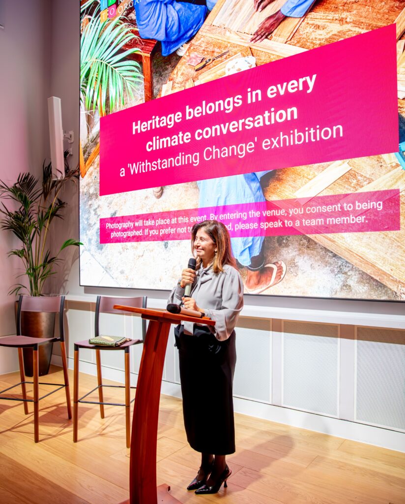 A woman giving a speech in front of a large screen with the title ‘Heritage belongs in every climate conversation’