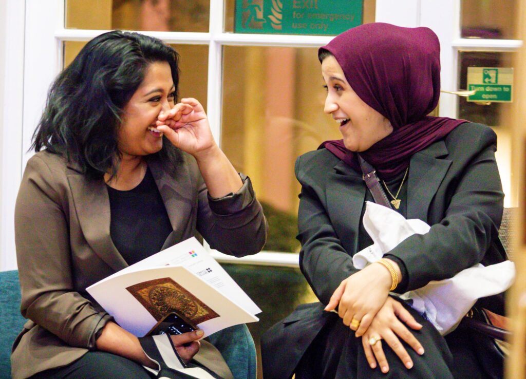 two women smiling and chatting -one is holding an exhibition guide