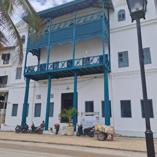 the facade of an historic building in Zanzibar. It is white with blue balconies and pillars across 3 stories of the building