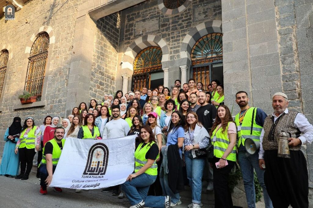 a large group of people posing in front of the theatre entrance holding a banner with the Turathuna logo