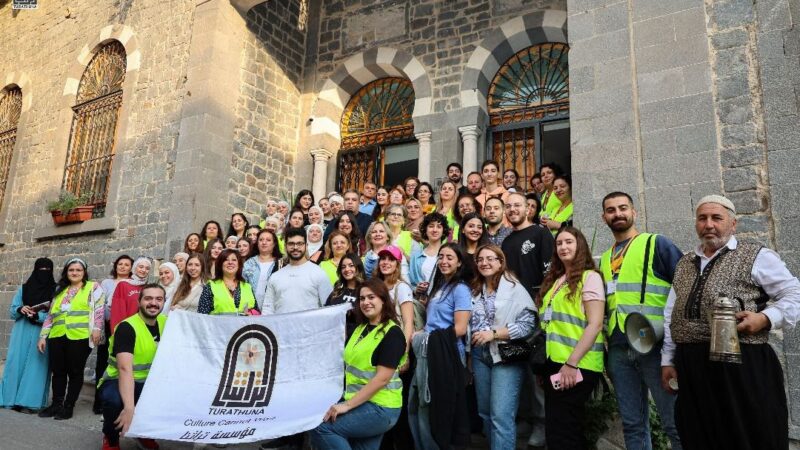 a large group of people posing in front of the theatre entrance holding a banner with the Turathuna logo