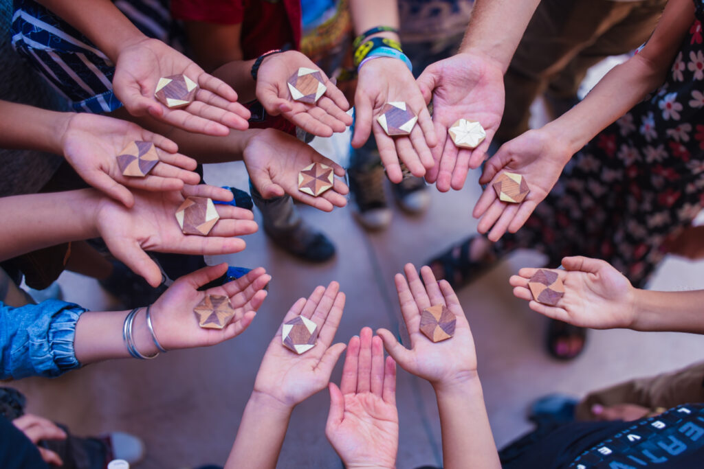 a circle of upturned children's hands, each holding a geometric wooden tile with Arabic designs
