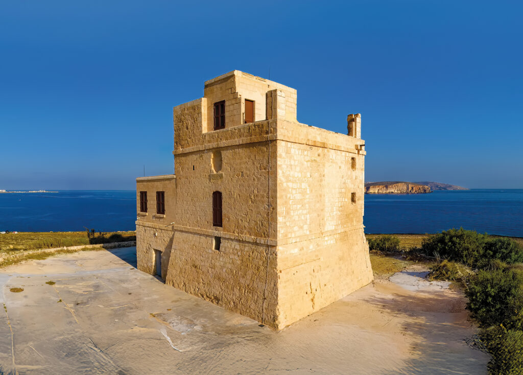 a pale stone defensive tower on the coast of Malta with blue skies and sea in the background