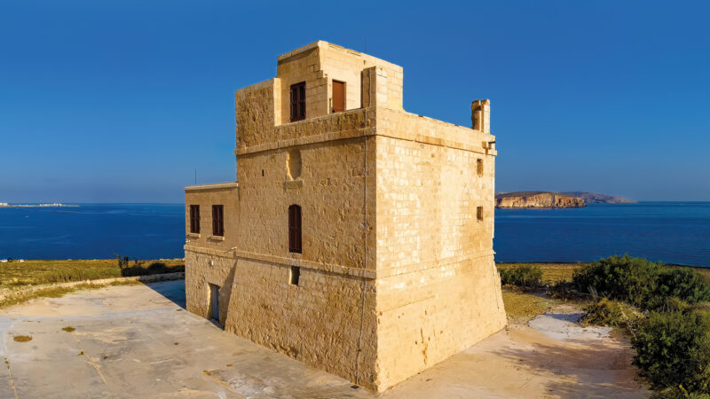 a pale stone defensive tower on the coast of Malta with blue skies and sea in the background