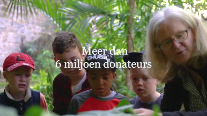 a white woman speaking to 4 children in a green natural setting as part of a nature workshop. There is white text overlaid in Dutch languages