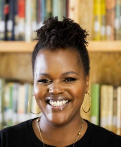 a headshot of a woman in a library smiling broadly